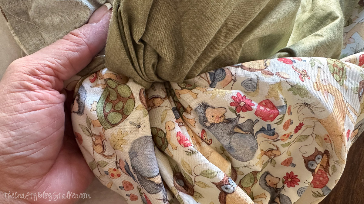 Hand turning a baby blanket right side out, showing green fabric backing and woodland animal print.