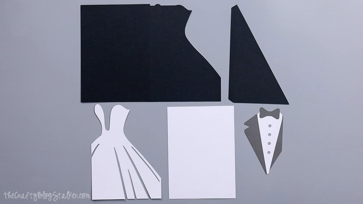 Cut cardstock pieces for a bride and groom wedding card, including dress, tuxedo, card base, and layered panels arranged on a table.