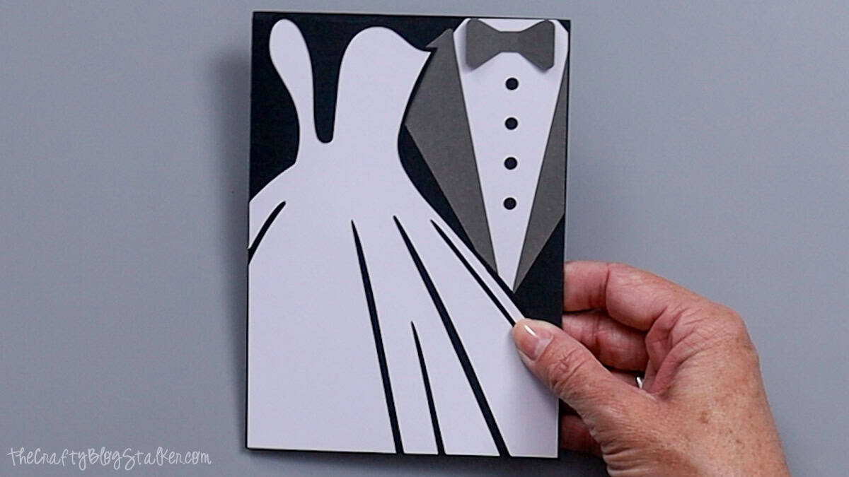 Finished handmade wedding card with a white bride dress and layered groom tuxedo design on a black cardstock background.