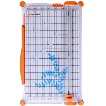 Paper cutter with measurement grid and sliding blade, shown from above with a small leaf design on the cutting surface.