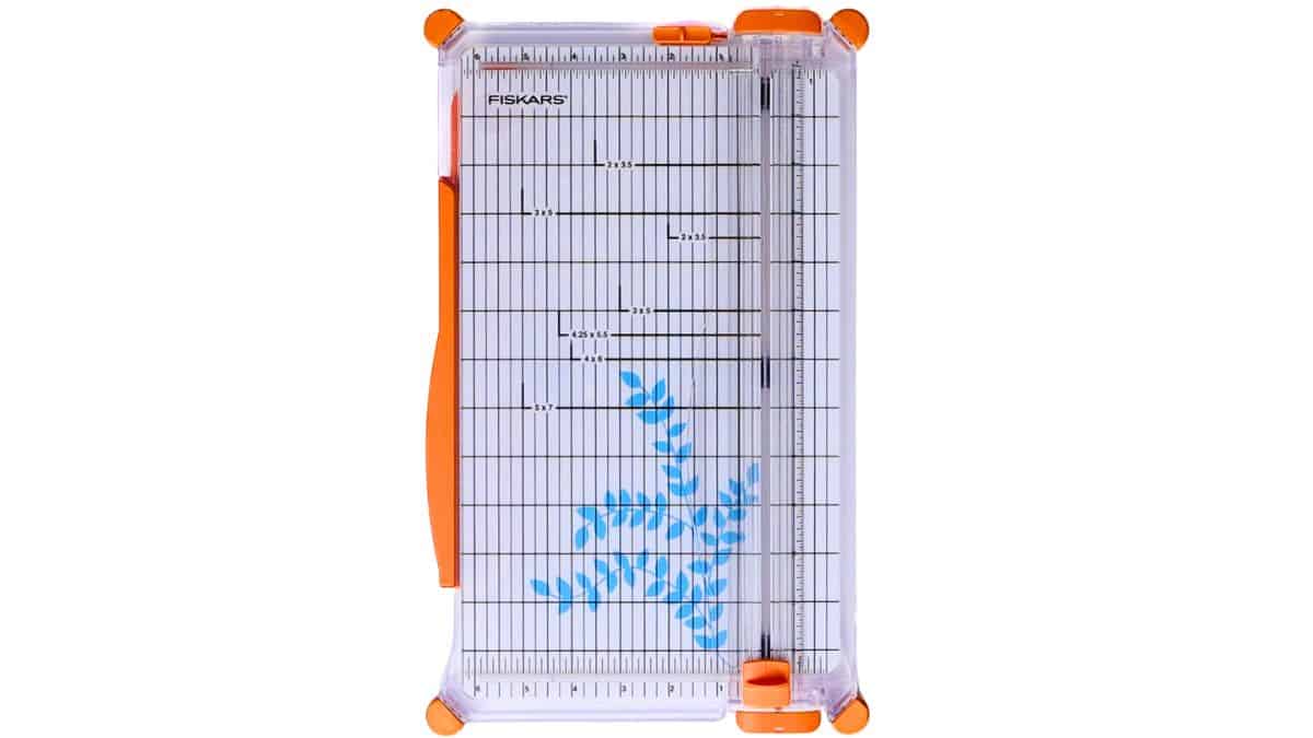 Paper cutter with measurement grid and sliding blade, shown from above with a small leaf design on the cutting surface.