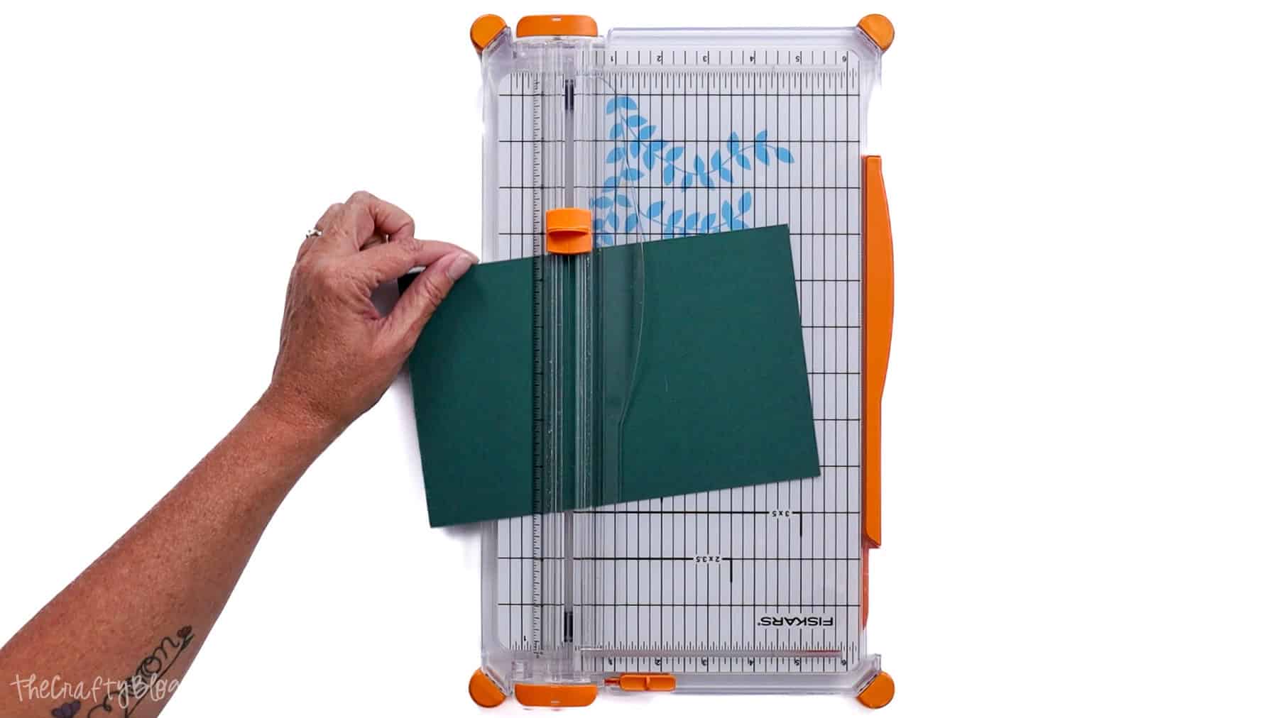 Hand cutting cardstock at an angle on a paper cutter, showing misaligned paper and an uneven trim.