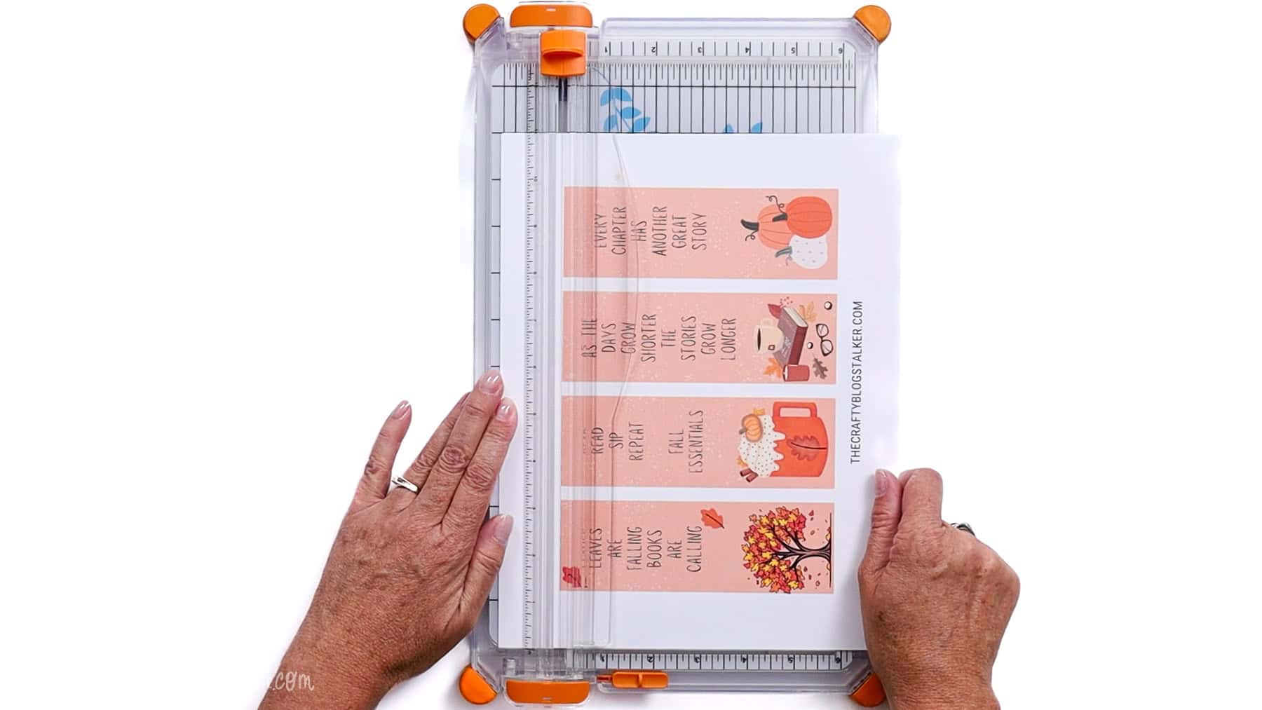 Hands aligning printed bookmarks on a paper cutter using the guide and sliding blade to make a straight, precise cut.