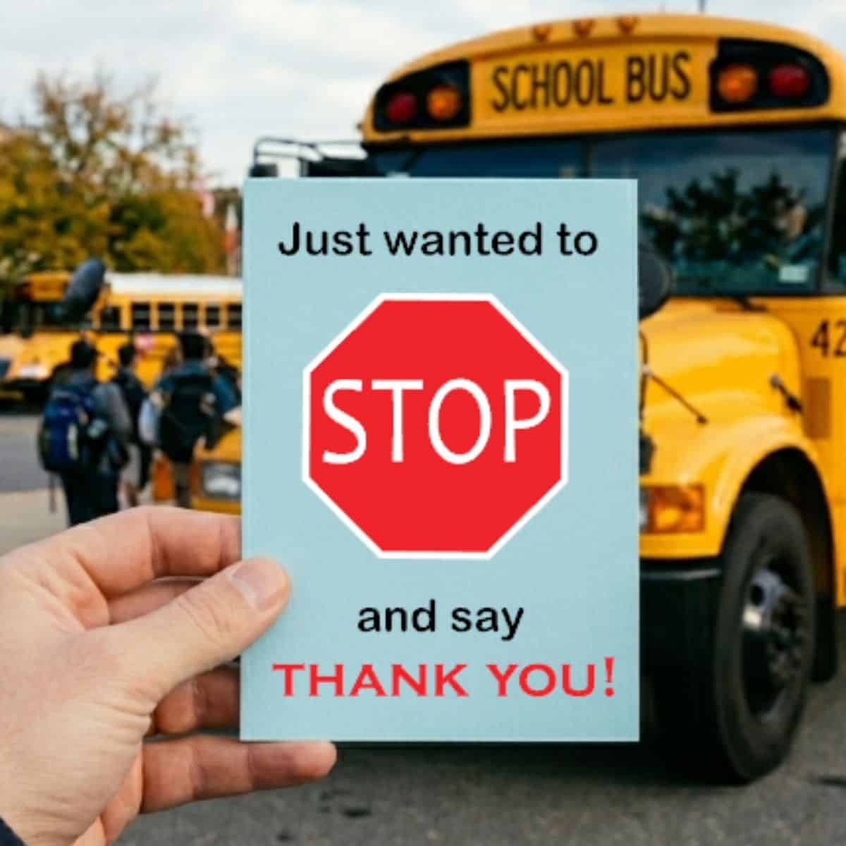 Hand holding a thank-you card with a stop sign graphic in front of a yellow school bus and students, reading 