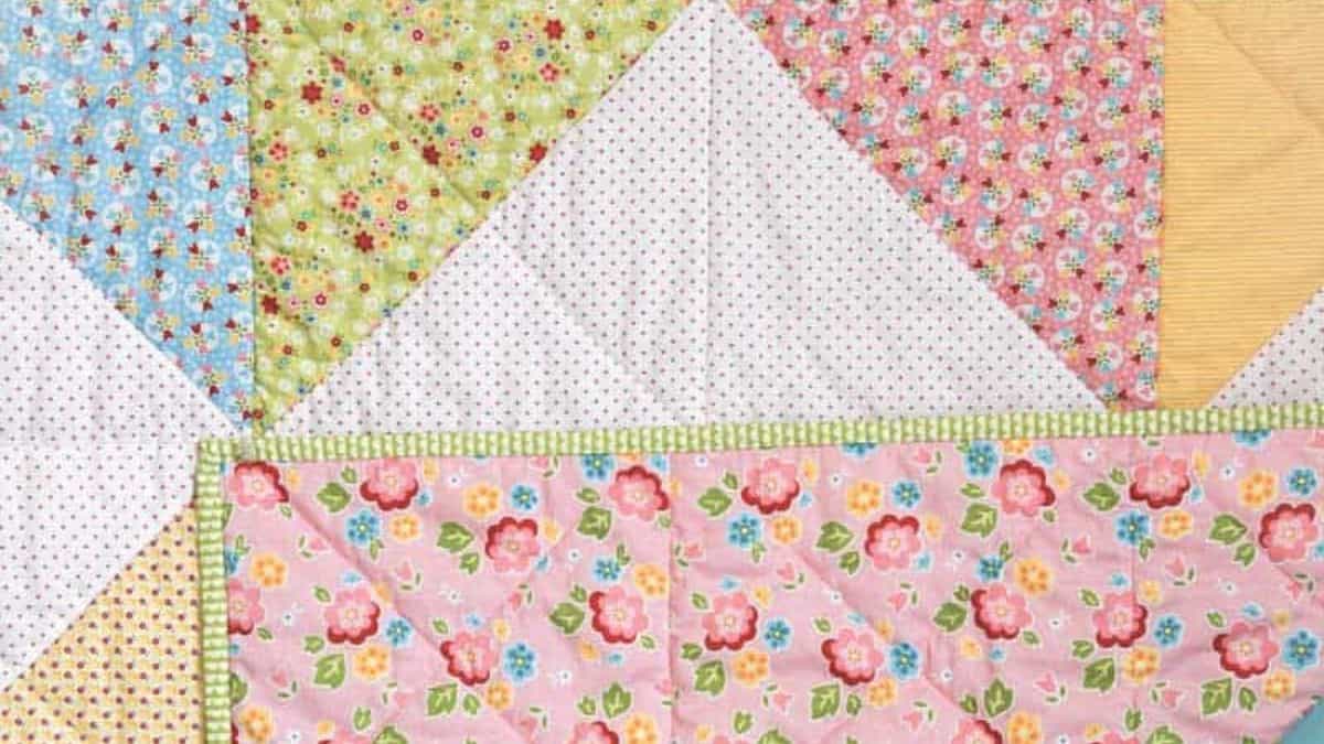 Close-up of a patchwork quilt with colorful floral and patterned fabric squares, showing front and folded back layers with stitched quilting details