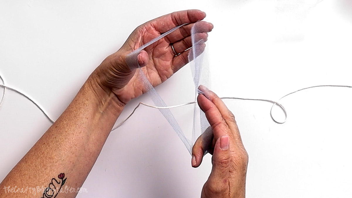 Hands tying a strip of light blue tulle onto a string to create a fluffy garland for a birthday banner.