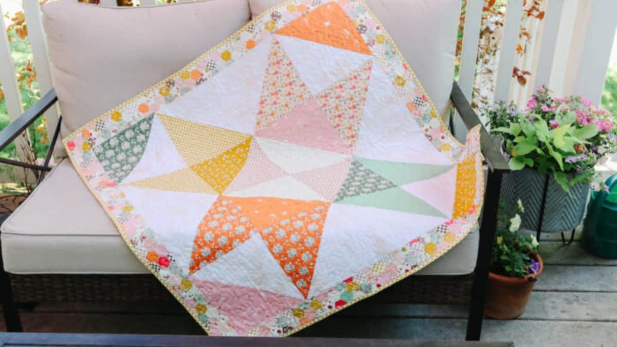 Colorful star quilt with pastel and floral fabrics draped over a cushioned outdoor chair, featuring large star blocks and a patterned border