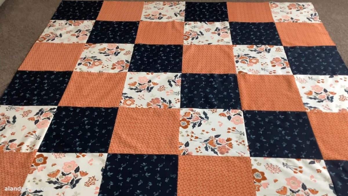 Checkerboard patchwork quilt with navy, peach, and floral fabric squares arranged in a grid pattern, laid flat on a surface