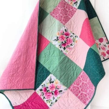 Patchwork quilt with pink, green, and floral fabric squares draped over a chair, showing stitched quilting lines and soft texture