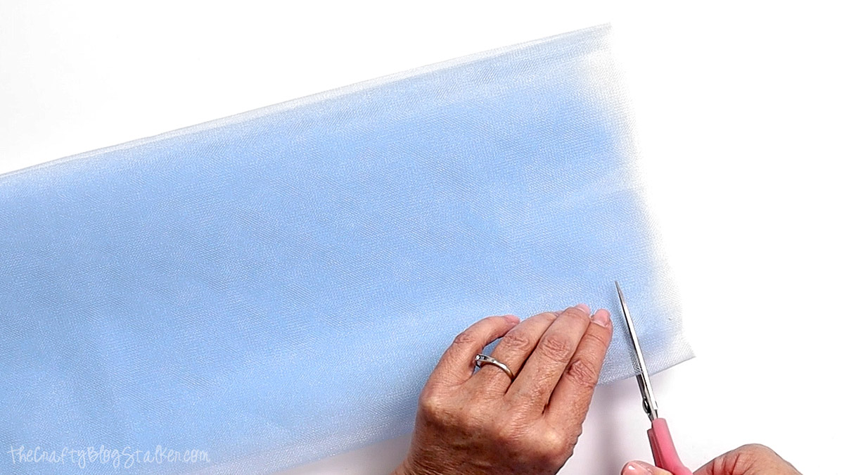 Hands cutting light blue tulle into strips with scissors for a DIY banner or decoration.