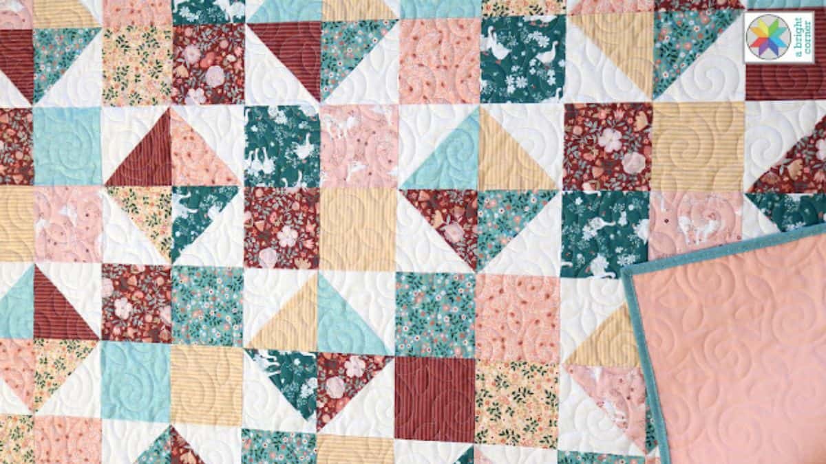 Colorful patchwork quilt with four-patch and triangle blocks in teal, coral, yellow, and cream fabrics, showing swirling quilting details and a folded corner