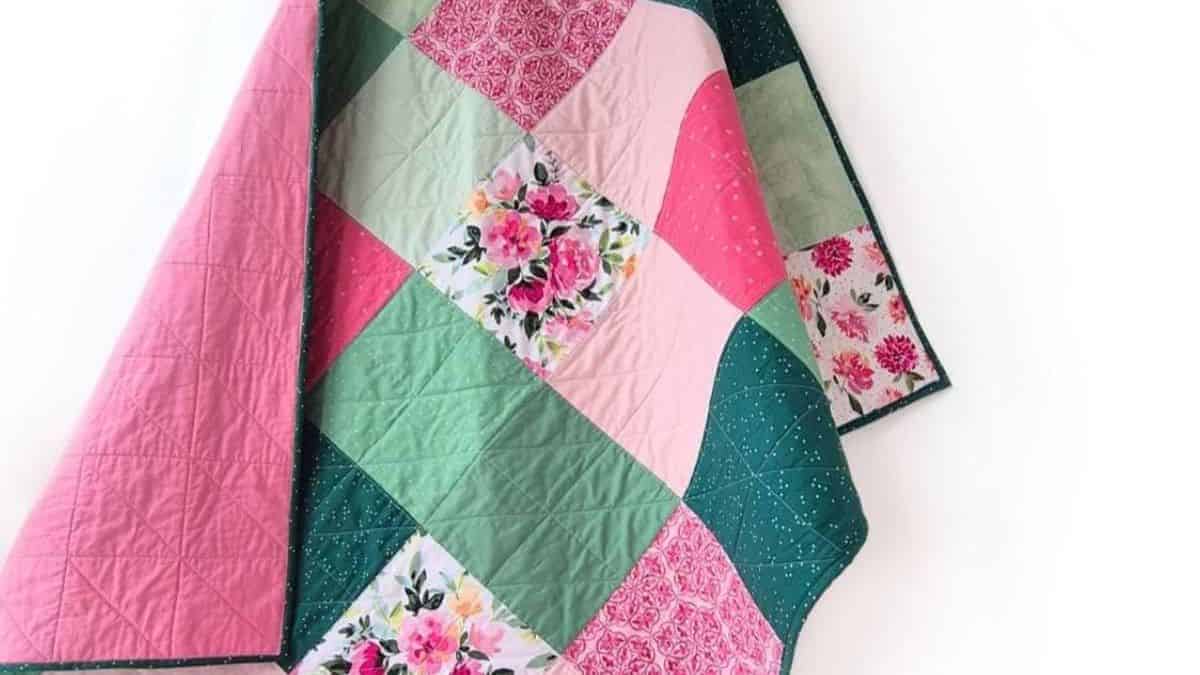 Colorful patchwork quilt with pink, teal, and floral fabric squares arranged in a diamond pattern, draped against a white background