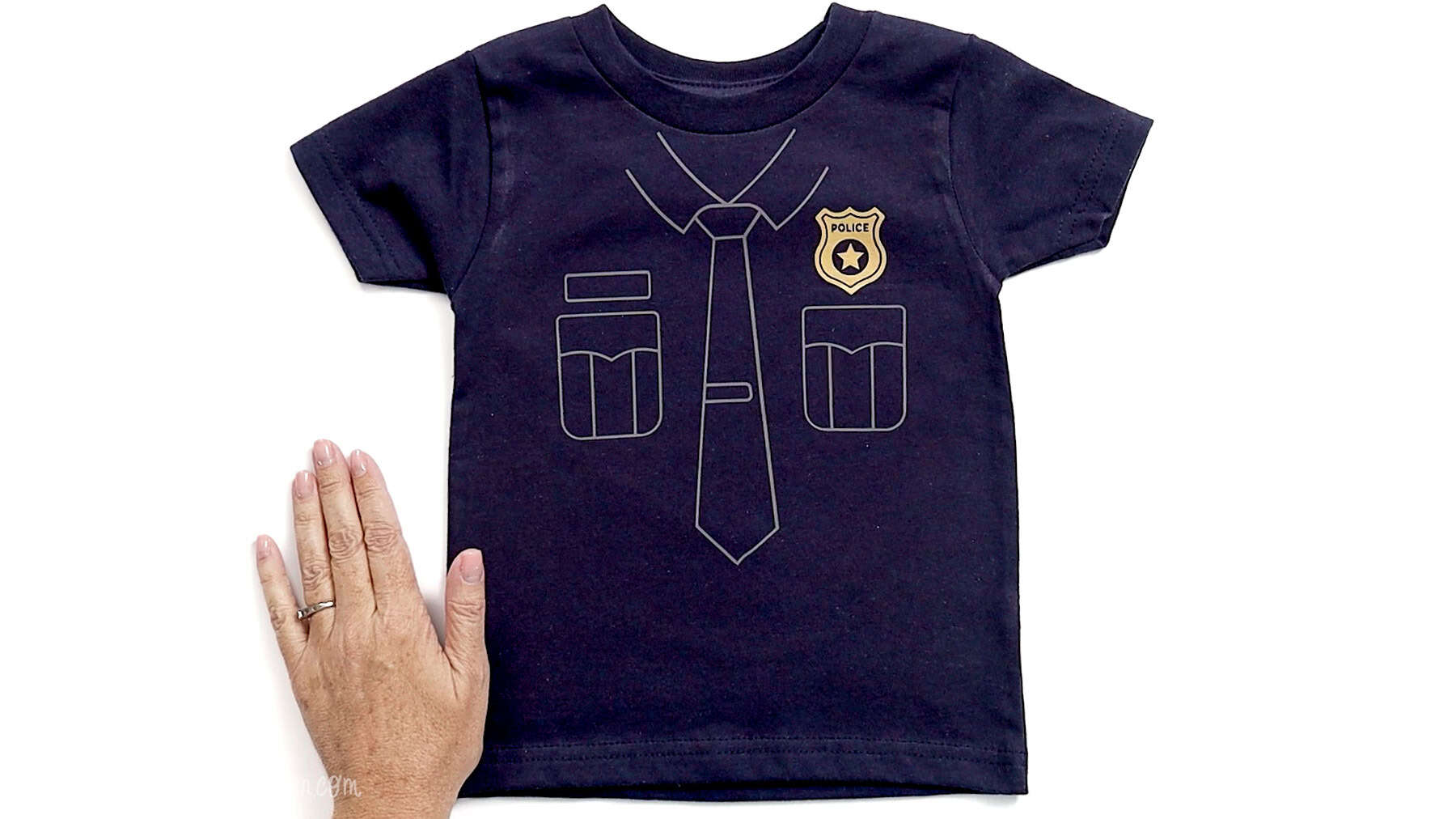 Finished navy toddler shirt with white police uniform vinyl design and badge applied, displayed flat with a hand beside it