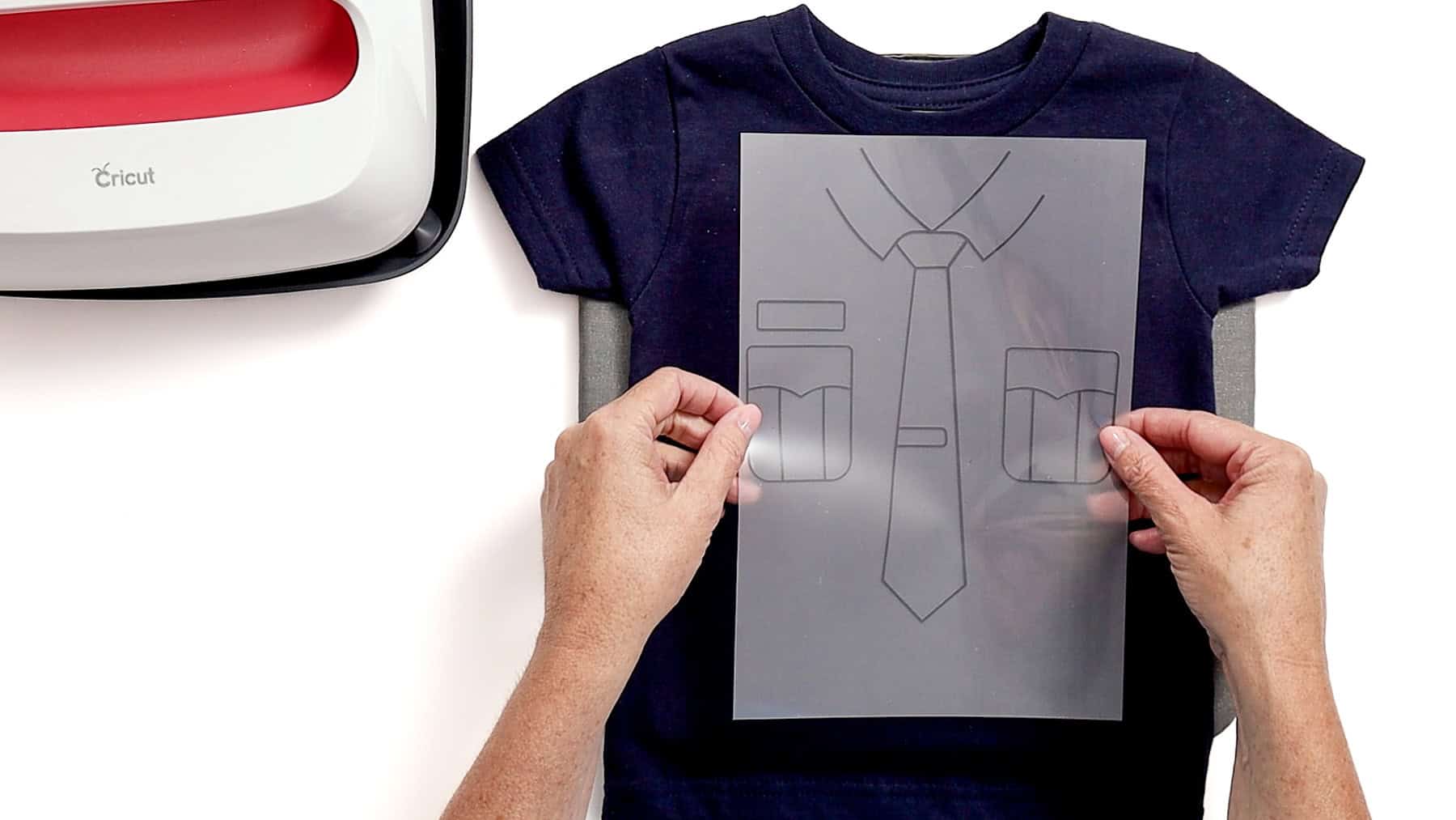 Hands placing a clear carrier sheet with a police uniform vinyl design onto a navy toddler shirt, ready for heat pressing with a Cricut machine