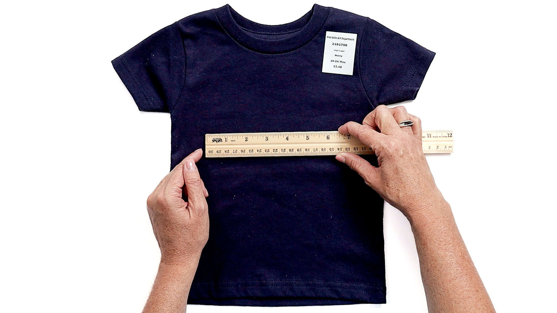 Hands measuring the width of a navy toddler T-shirt with a ruler laid across the chest, preparing for a Cricut design placement
