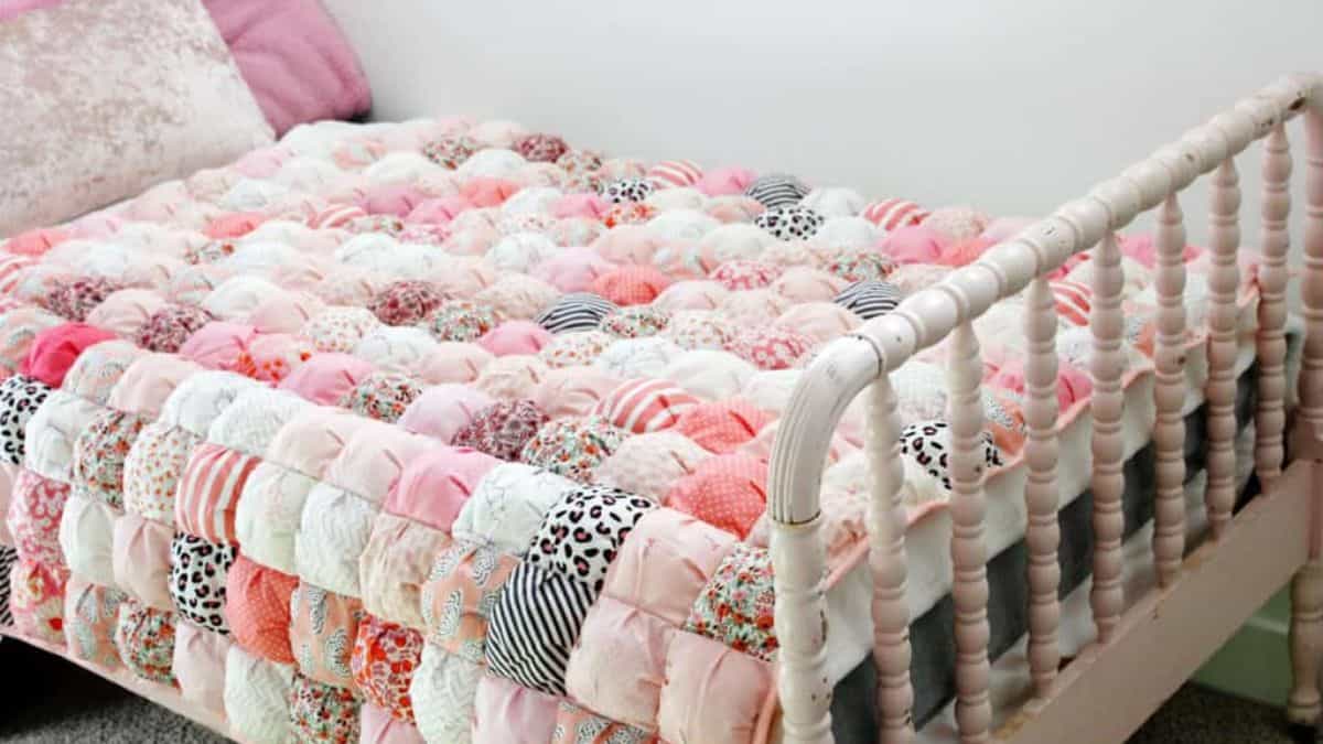 Puff quilt with soft pink, white, and patterned fabric squares arranged in a textured bubble design on a bed with a white wooden frame
