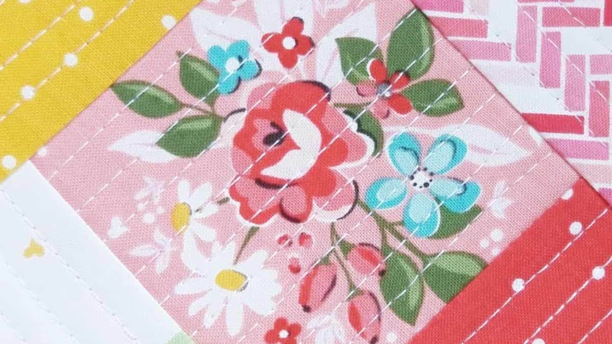 Close-up of quilt blocks with pink floral fabric, geometric patterns, and visible stitching lines showing a quilt-as-you-go design technique