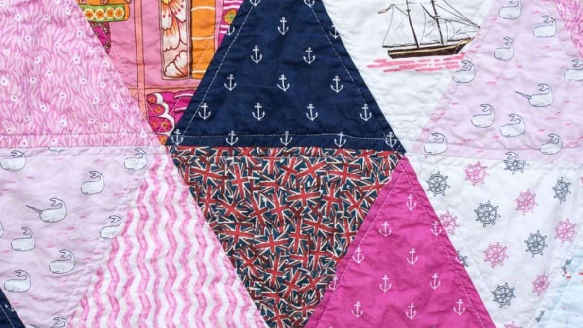 Close-up of a triangle patchwork quilt with pink, navy, and patterned fabrics, including anchors, swans, ships, and geometric prints stitched together