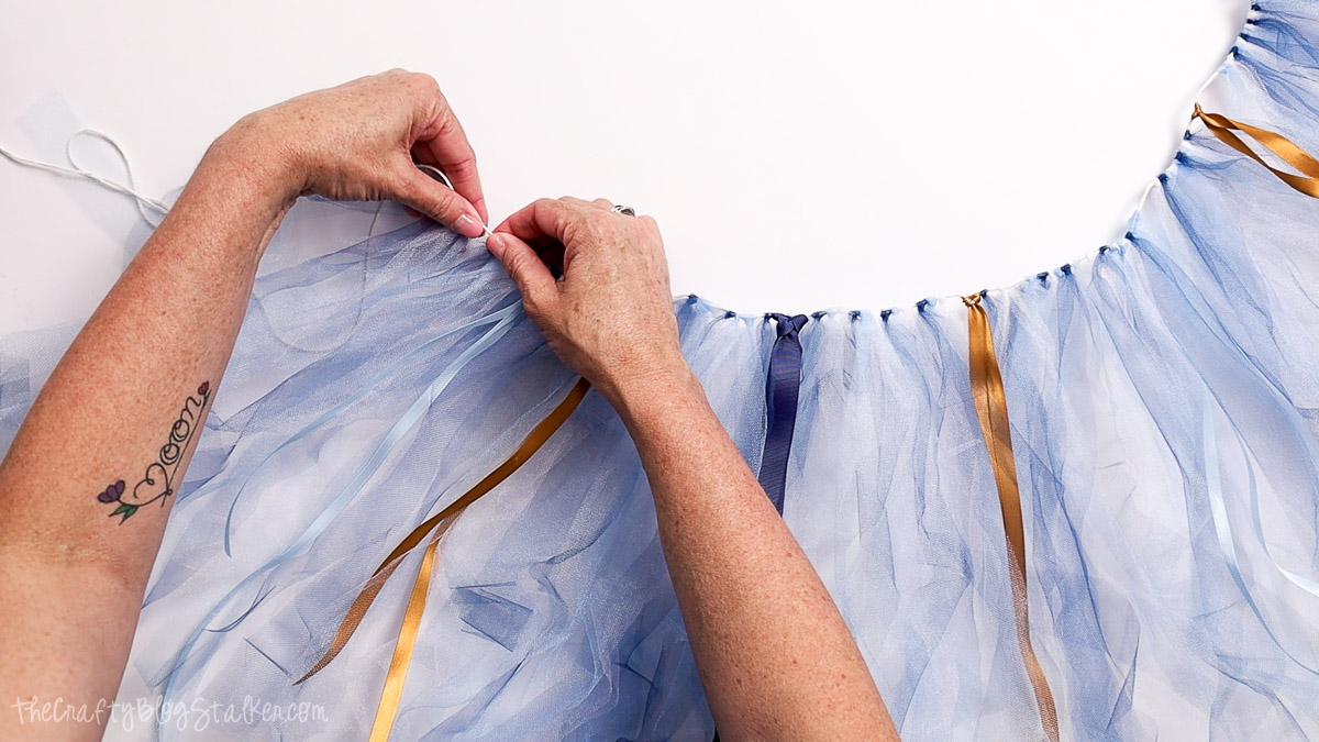 Hands tying light blue tulle and gold ribbon onto a string to create a fluffy garland for a first birthday high chair banner.
