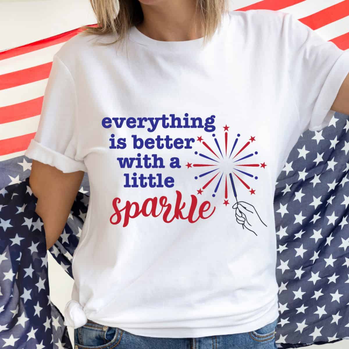 Woman wearing a white patriotic T-shirt with everything is better with a little sparkle graphic and red, white, and blue fireworks design.