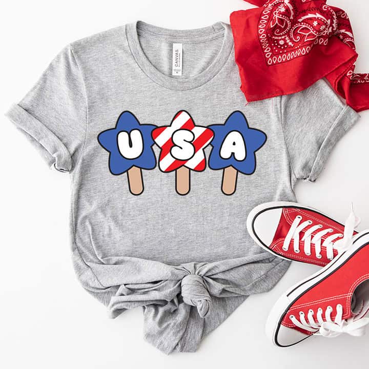 Gray patriotic T-shirt with USA popsicle graphic styled with red sneakers and a red bandana on a light background.