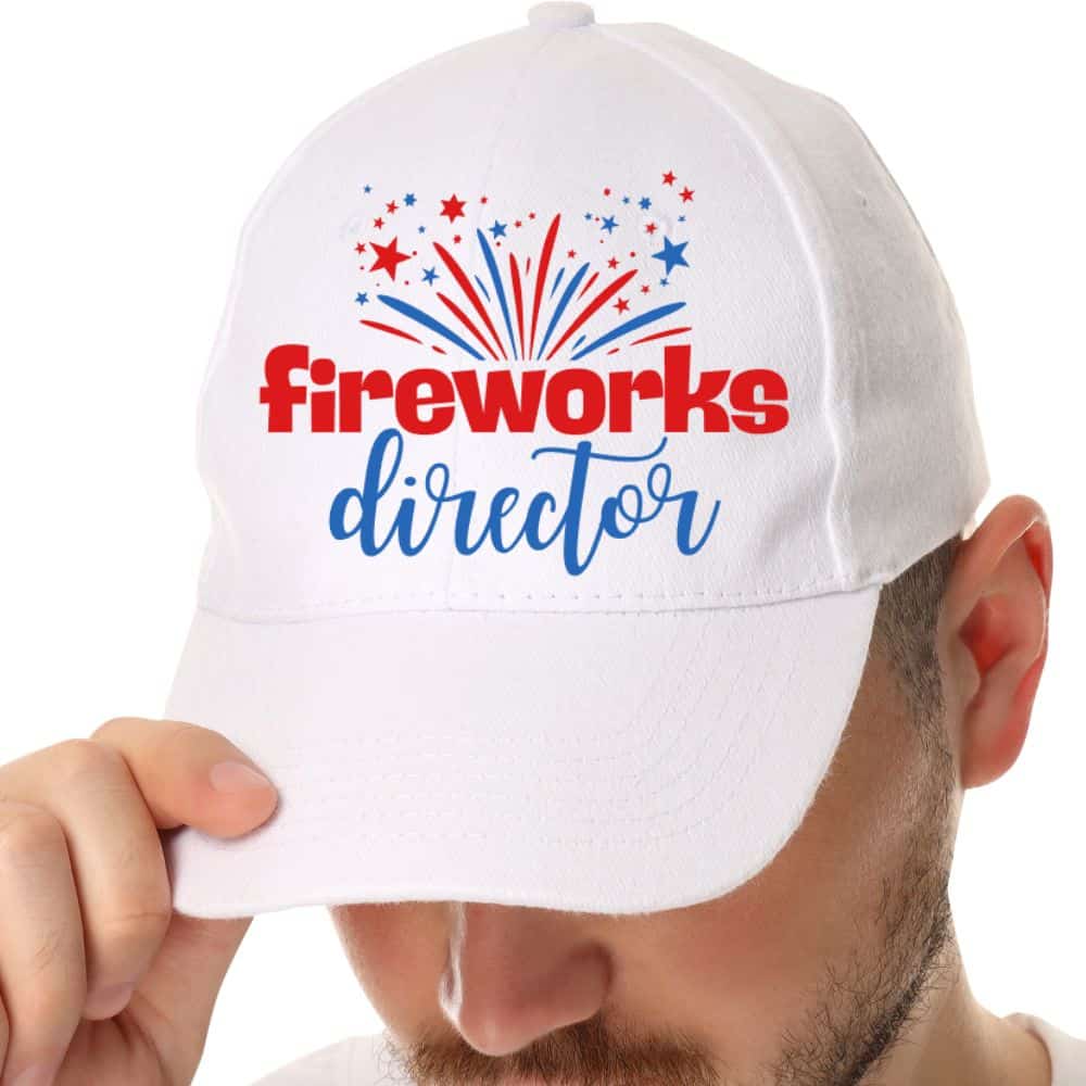 Man wearing a white baseball cap with fireworks director patriotic design in red and blue lettering and fireworks graphics.