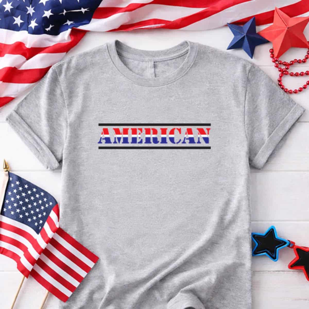 Gray patriotic T-shirt with the word American in red, white, and blue lettering surrounded by flags and festive decorations.