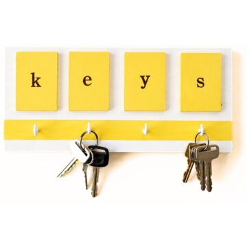 Yellow and white wall-mounted key holder with tiles spelling “keys” and four hooks holding sets of keys.
