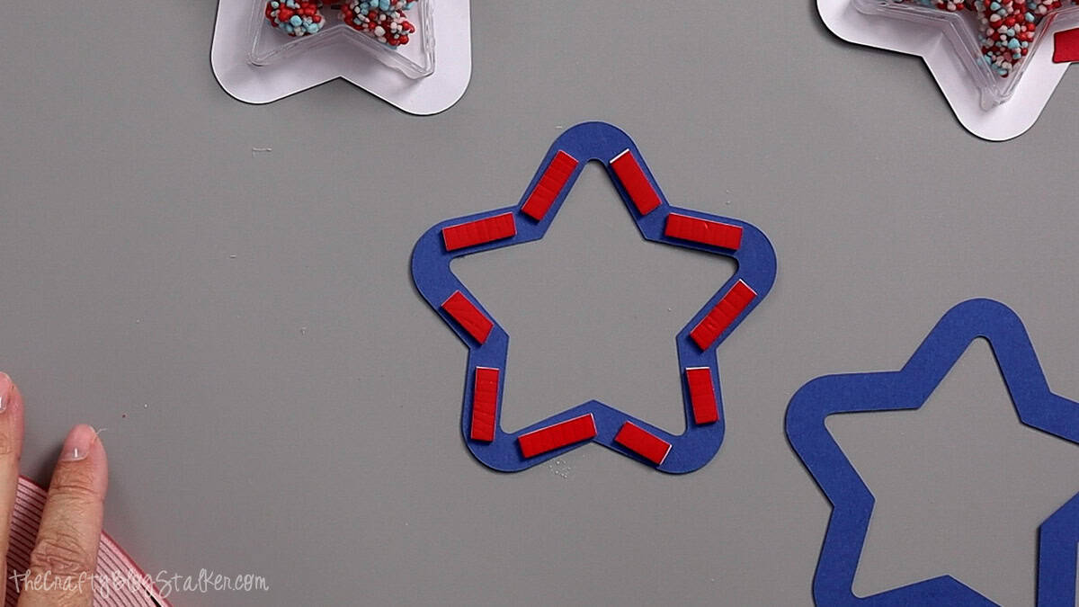 Blue star-shaped paper cutout with red foam adhesive strips placed around the edges for a patriotic shaker party favor craft.