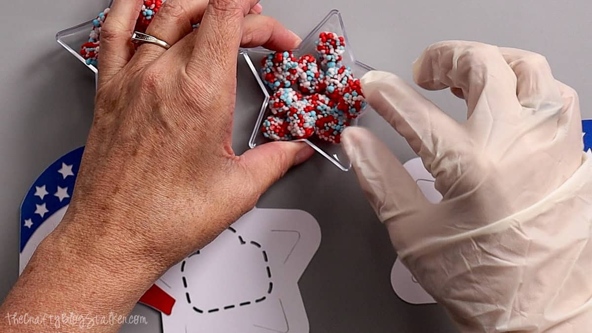 Hands filling clear star ornaments with red, white, and blue candy for patriotic party favors.