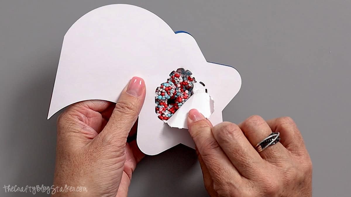 Hands peeling back the paper opening on a patriotic star shaker party favor filled with red, white, and blue candy sprinkles.