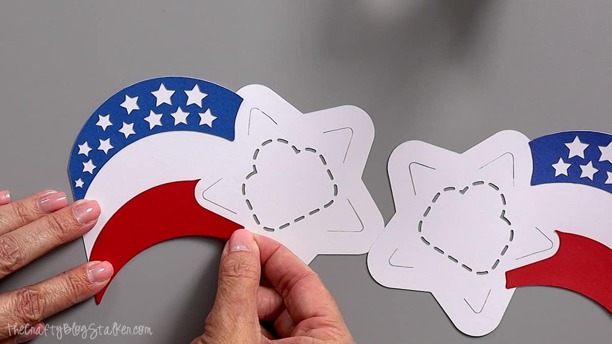 Hands layering red, white, and blue cardstock pieces to assemble patriotic star party favors.