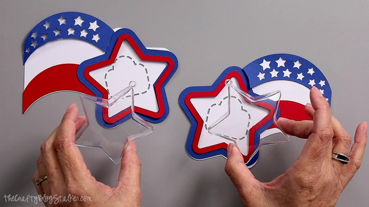 Hands holding clear star ornaments next to layered red, white, and blue patriotic paper party favor pieces.