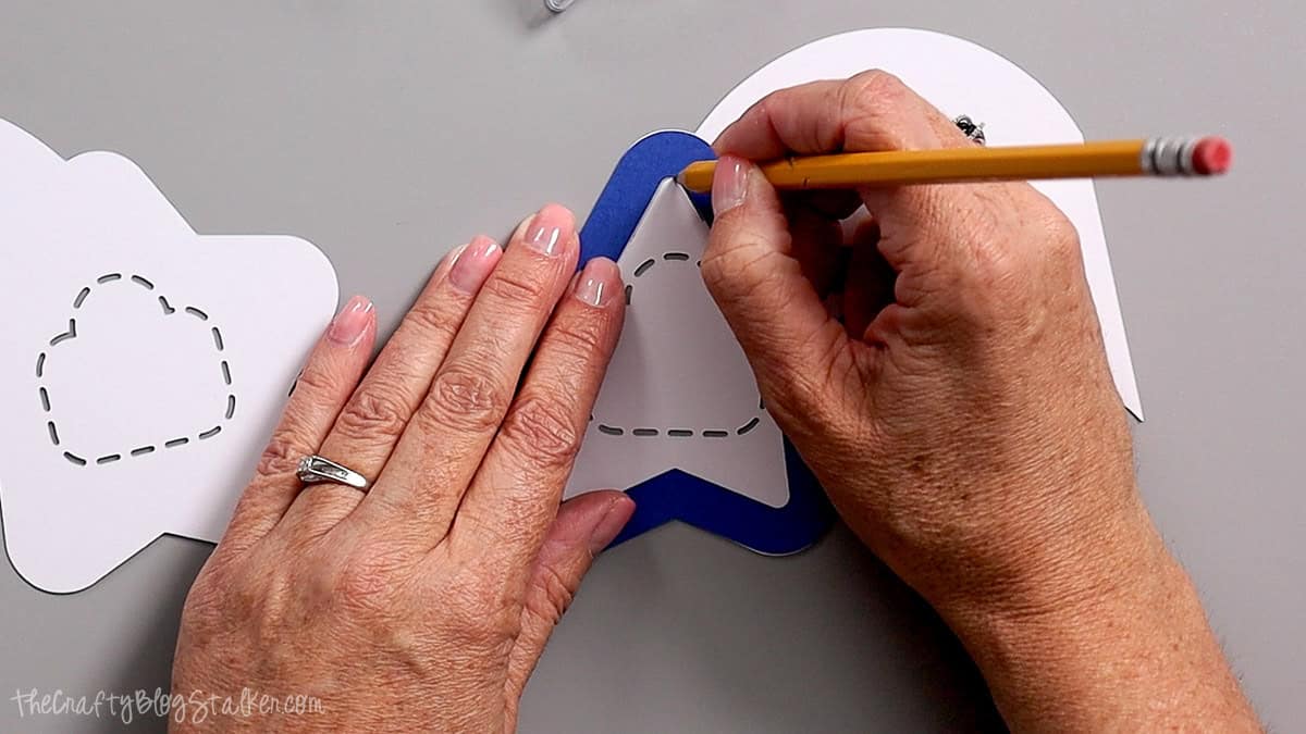 Hands tracing a star template onto patriotic cardstock pieces for a DIY Fourth of July party favor craft.