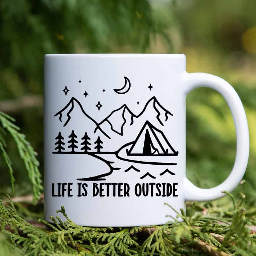 White ceramic mug with a black camping design featuring mountains, trees, a tent, moon, and the phrase