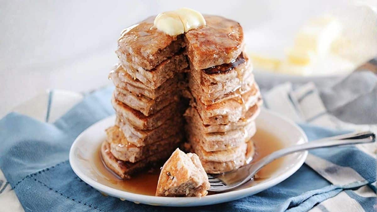 Stack of fluffy cinnamon pancakes topped with butter and maple syrup, served on a white plate with a fork and blue napkin.