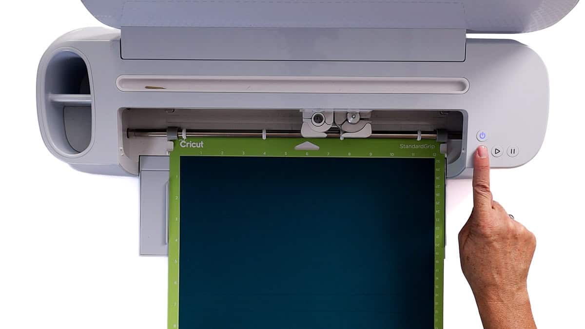 Person loading a Cricut cutting mat with dark blue iron-on vinyl into a Cricut machine and pressing the load button.