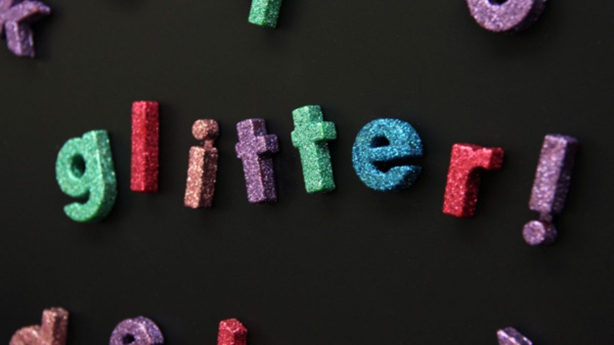 Colorful glitter letter magnets spelling “glitter!” on a black background, showcasing a fun DIY craft project with sparkling foam letters.