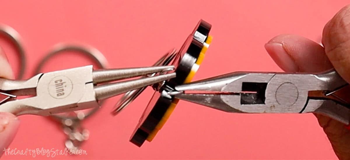 Close-up of pliers attaching a jump ring and key ring to a flower-shaped resin keychain during the final assembly step.