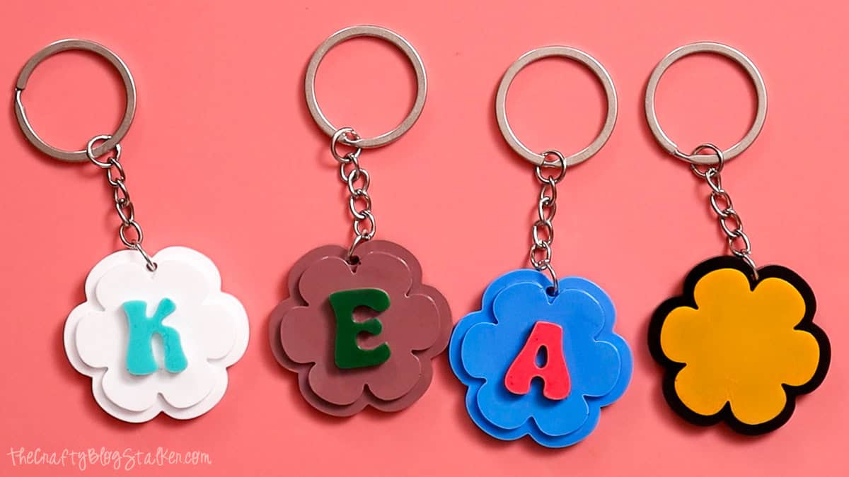 Finished flower-shaped resin keychains with colorful letters attached to silver key rings displayed on a pink background.