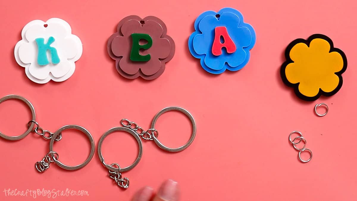 Flower-shaped resin keychain pieces, key rings, and jump rings arranged on a pink background before assembling personalized resin keychains.