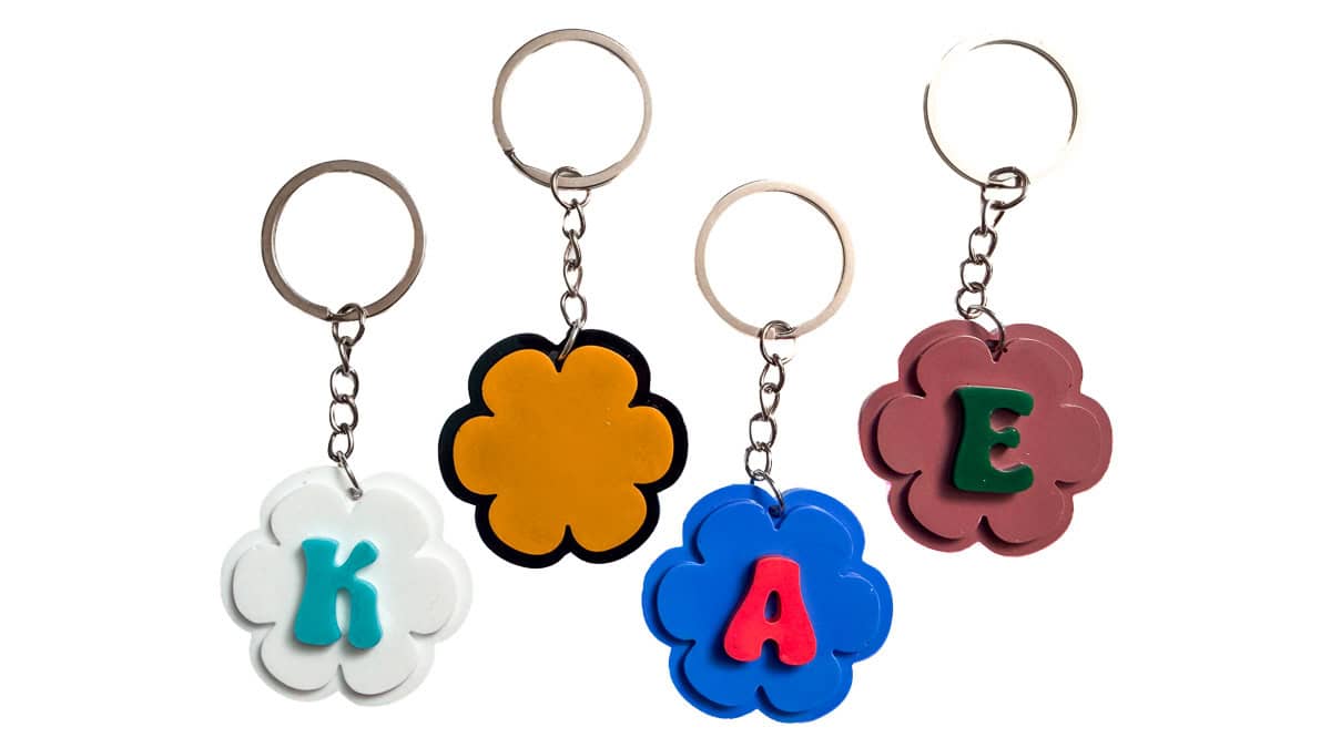 Four colorful flower-shaped resin keychains with letter initials and metal key rings displayed on a white background.