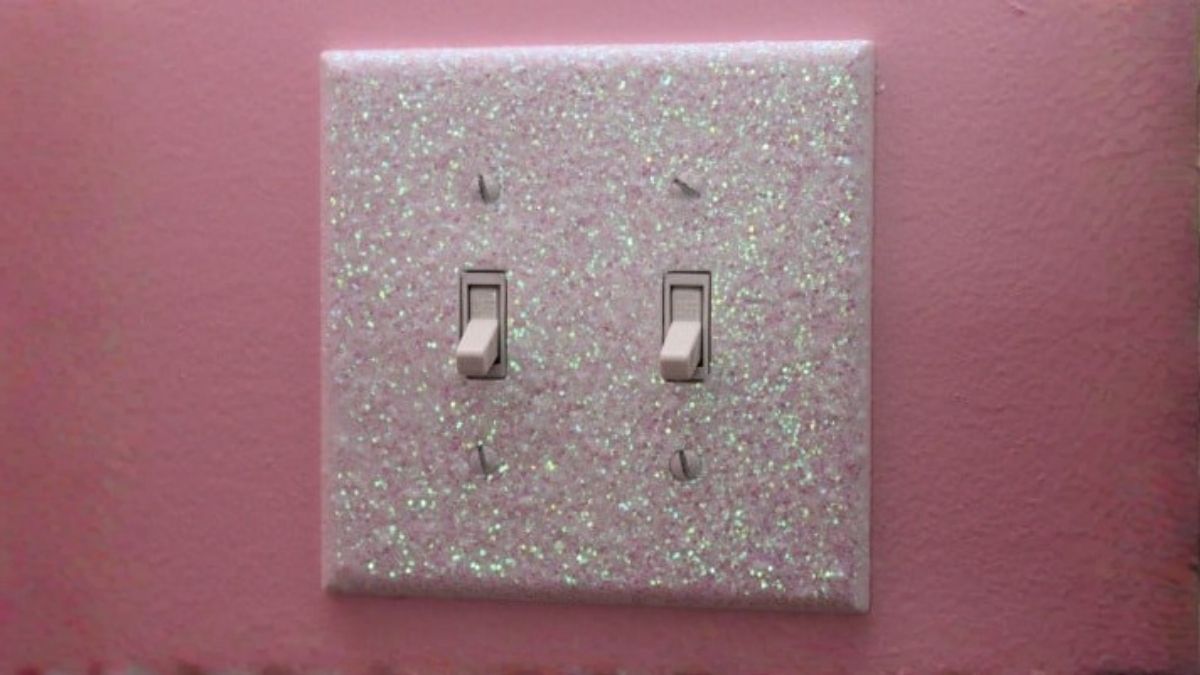 Pink glitter light switch plate with two toggle switches mounted on a pink wall, adding a sparkling decorative accent to the room.