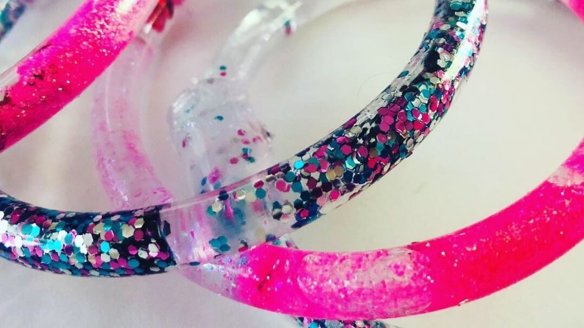 Close-up of clear plastic tube bracelets filled with pink and multicolor glitter, creating fun, sparkly DIY jewelry.
