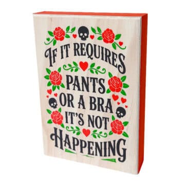 Whitewashed wood sign with black lettering, red roses, green leaves, hearts, and skulls that reads, If It Requires Pants or a Bra It's Not Happening.