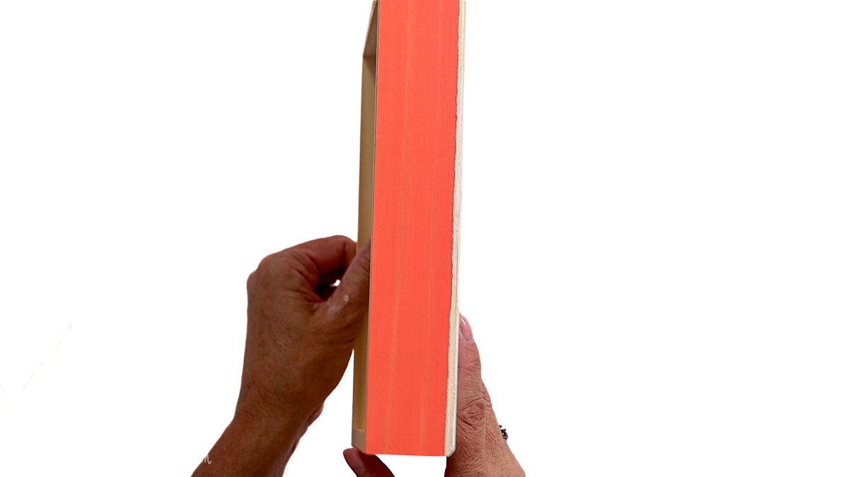 Hand holding a wood sign with freshly painted coral edges, creating a colorful border for a DIY heat transfer vinyl wood sign.