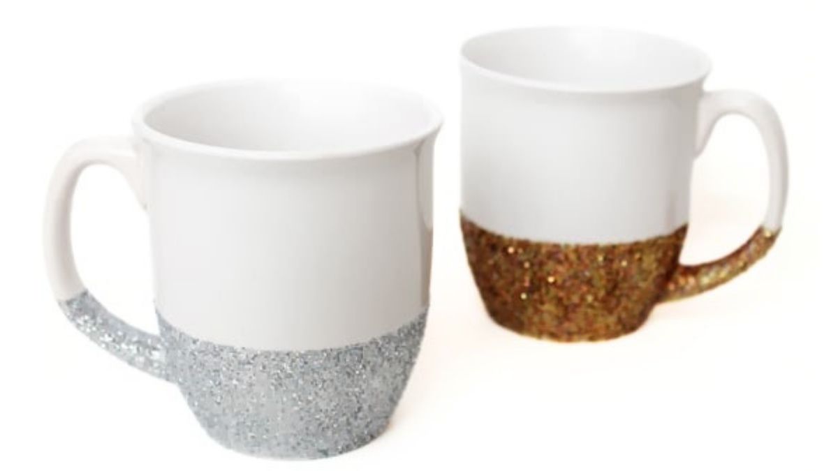 Two white ceramic mugs with glitter-dipped bottoms and handles, one silver and one gold, displayed as DIY dishwasher-safe glitter mugs.