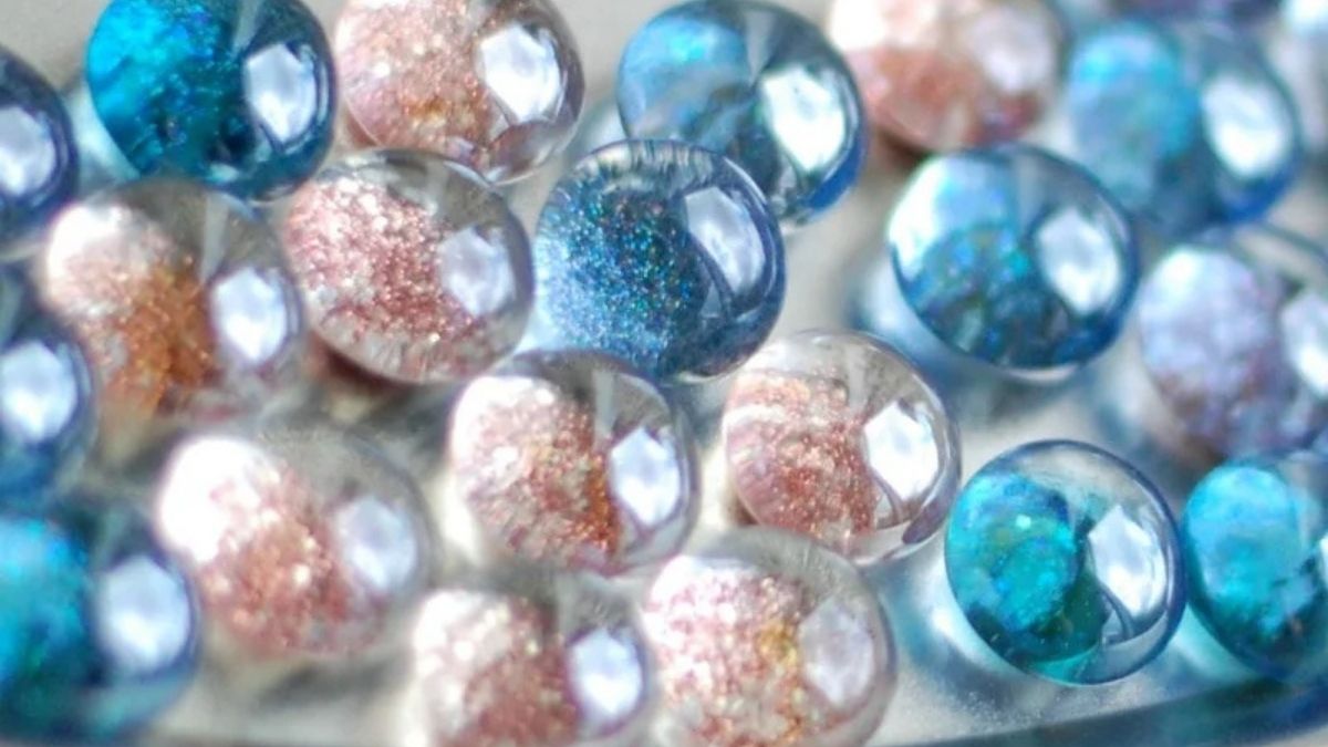 Close-up of round glass glitter magnets in blue and pink tones with sparkling centers, arranged together on a white surface.