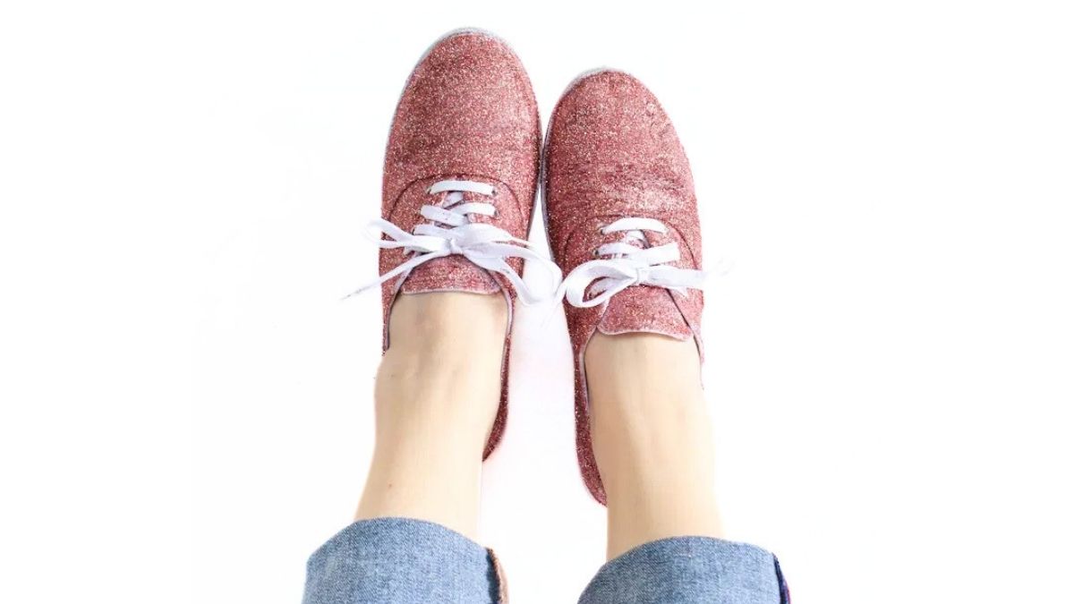 Pink glitter lace-up shoes with white laces worn with rolled-up jeans, photographed from above on a white background.