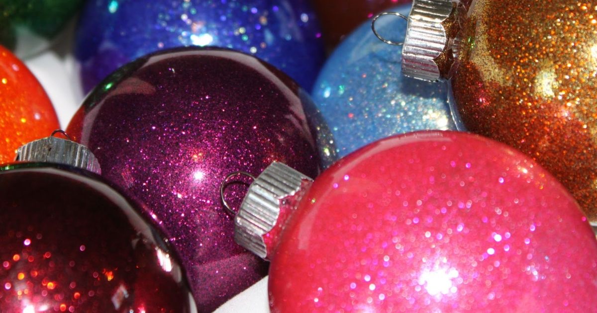 Close-up of colorful glitter Christmas ornaments in pink, purple, blue, orange, and gold with sparkling finishes and silver ornament caps.